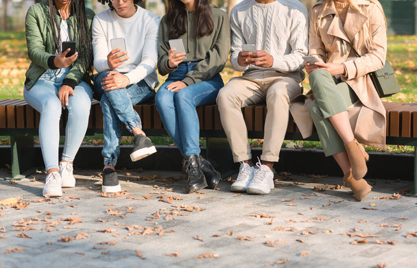 Cortado de jovens amigos usando telefones celulares, sentado no banco - Foto, Imagem