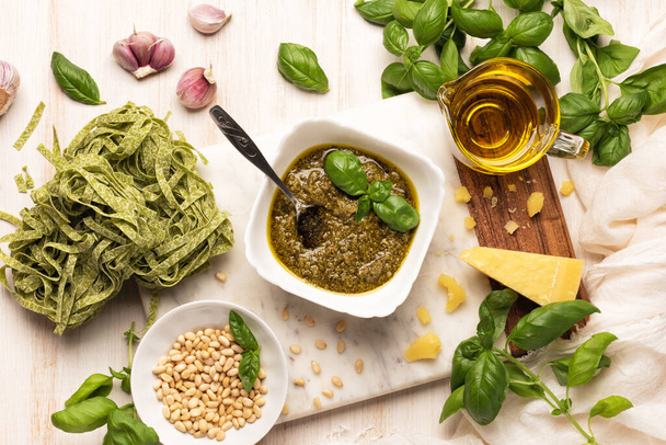 Makarnalı pesto, taze fesleğen, sarımsak, parmesan peyniri, çam fıstığı ve mermer tahtada zeytinyağı. İtalyan soslu ahşap mutfak masası - Fotoğraf, Görsel