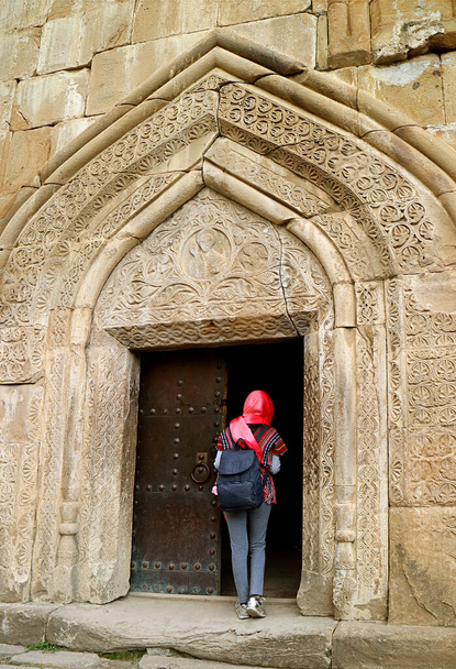 Femme voyageuse en couverture de tête à l'entrée de l'église de l'Assomption dans le complexe du château d'Ananuri, rive de la rivière Aragvi, Géorgie - Photo, image