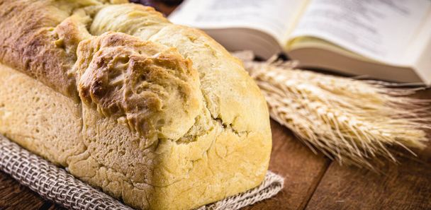 zelfgemaakt brood gemaakt in de Paas- en Eucharistieperiode, genaamd Christusbrood, religieus symbool, met Bijbel en kruisbeeld op de achtergrond - Foto, afbeelding