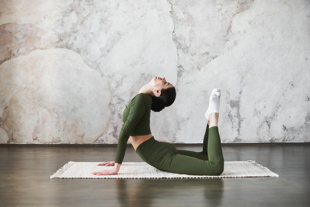 Portrait of young attractive woman wearing sportswear, start her day doing stretching practice, doing exercise for spine flexibility, doing yoga or pilates exercise, King Cobra Pose,Raja bhudjangasana - 写真・画像