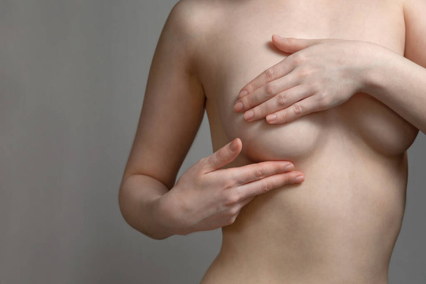 A young woman conducts an independent examination for the presence of tumors in the breast. Gray background. The concept of women's breast diseases. Copy space. - Foto, afbeelding