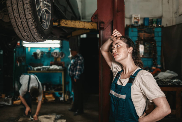 The concept of small business, feminism and women's equality. A young female auto mechanic wearily wipes sweat from her forehead. - Photo, Image