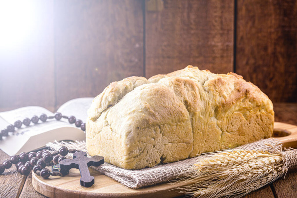 domácí chléb vyrobený v době Velikonoc a eucharistie, zvaný Kristův chléb, náboženský symbol, s biblí a krucifixem v pozadí - Fotografie, Obrázek