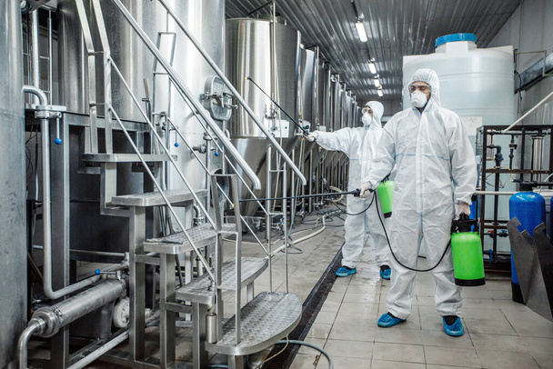 Men in protective suits with green spray bags disinfect plant - Zdjęcie, obraz