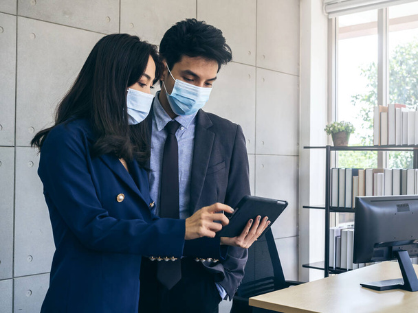 Azjatycki biznes mężczyzna i kobieta w garniturze i ochronne maski twarzy przy użyciu tabletu cyfrowego, spotkanie i współpraca w biurze, nowy normalny styl życia po zamknięciu pandemii koronawirusowej. - Zdjęcie, obraz