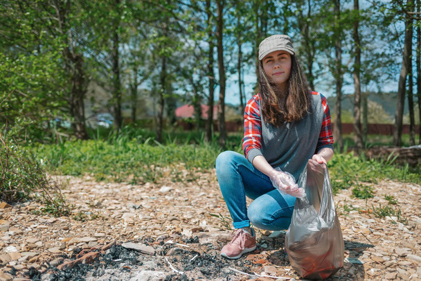 A young female volunteer collects garbage in the picnic area. The concept of earth day and ecology and environmental conservation. - Photo, Image