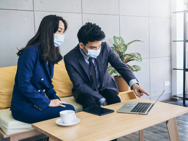 Azjatycki biznes mężczyzna i kobieta w garniturze i ochronne maski twarzy za pomocą komputera na biurku, spotkanie i współpraca w biurze, nowy normalny styl życia po zamknięciu pandemii koronawirusa. - Zdjęcie, obraz