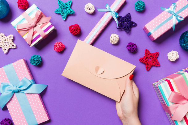 Top view of woman holding an envelope on purple background made of holiday decorations. Christmas time concept. - 写真・画像