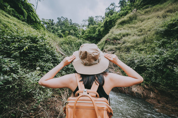 Rückseite der Reisefrau, die mit der Hand ihren Hut berührt, sich frei fühlt und beim Wandern die Natur in den Bergen genießt - Foto, Bild