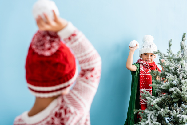 帽子に子供の選択的な焦点と青い上の弟と遊んでいる間に雪玉を保持スカーフ  - 写真・画像
