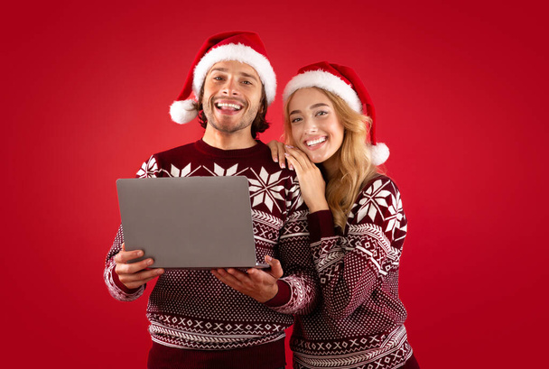 Online nyaralás vásárlás. Romantikus pár karácsonyi ruhák laptop számítógép piros háttér - Fotó, kép