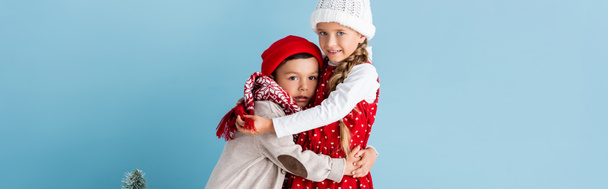 panoramic crop of kids in winter outfit hugging near christmas tree on blue - Fotó, kép