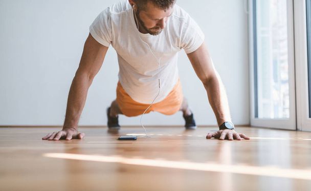 Handsome young man working out at home with a smart watch - Fotoğraf, Görsel