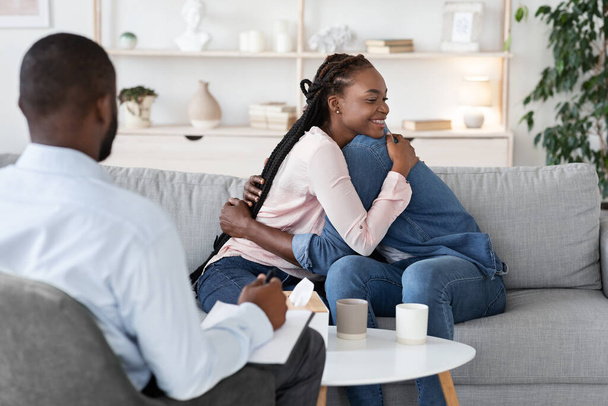 Koppeltherapie. Liefdevolle Afrikaanse echtgenoten knuffelen bij Family Counselors Office na verzoening - Foto, afbeelding