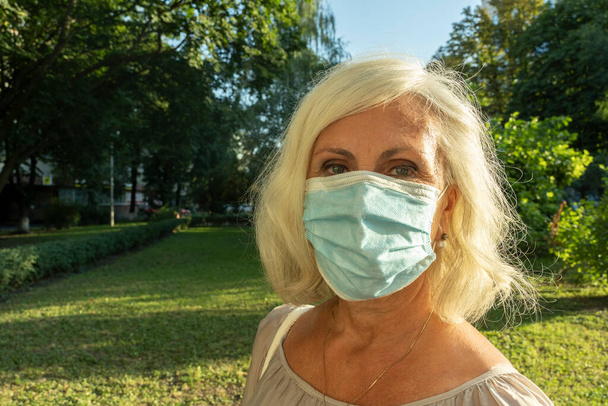close-up portret van grijs harige vrouw met gezichtsmasker. Vrouwelijke vrouw van middelbare leeftijd draagt gezichtsmasker buiten in het Corona virus COVID-19 pandemie - Foto, afbeelding