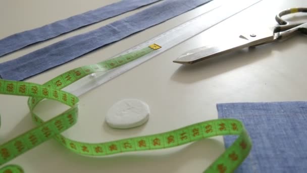 Kit de costura, tijeras de coser, trapos de tela azul, centímetro sobre un fondo de mesa blanco. Taller de costura, flujo de trabajo de fábrica de juguetes - Imágenes, Vídeo