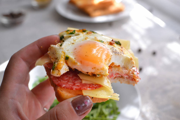 Tasty breakfast. Toast with egg, cheese and sausage. The girl holds a toast, a sandwich in her hand. Delicious food - Photo, image