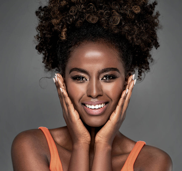 Beautiful african woman smiling and looking at camera with joy.  Beauty afro american girl with curly hair smiling, posing on gray studio background. - Φωτογραφία, εικόνα