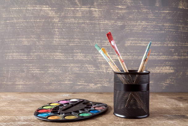 Watercolor palette and pot with brushes on  wooden background - Fotoğraf, Görsel