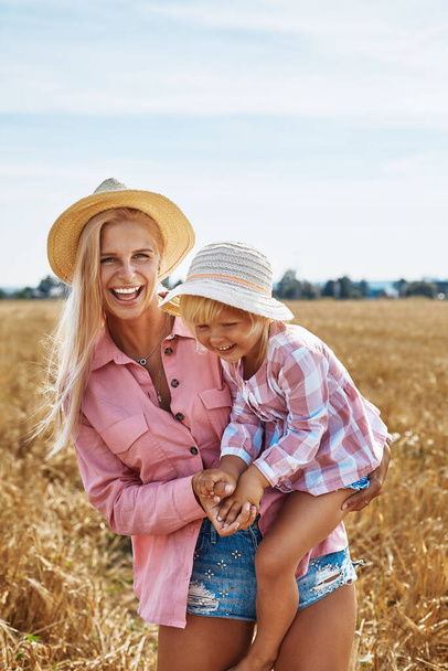 feliz madre sosteniendo al bebé sonriendo en un campo de trigo a la luz del sol - Foto, Imagen