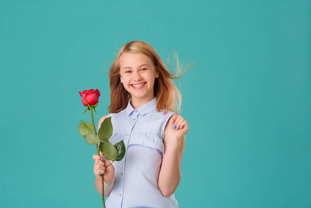 A happy laughing girl holds a red rose on a turquoise background - Fotoğraf, Görsel