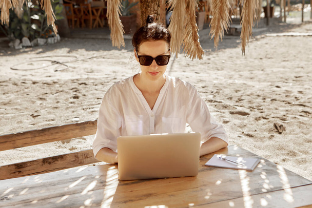 Mujer joven usando un ordenador portátil en una playa. Concepto de trabajo independiente - Foto, imagen