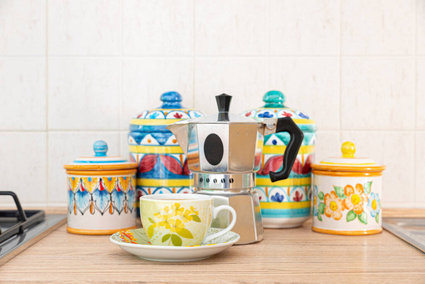 イタリアだ。キッチンカウンターの上には、美しくカラフルなヴェトナム陶器の瓶の前に置かれたコーヒーとコーヒーポットがあります。. - 写真・画像