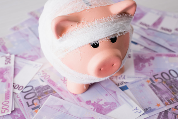Selective focus of piggy bank with bandage on money - Fotoğraf, Görsel