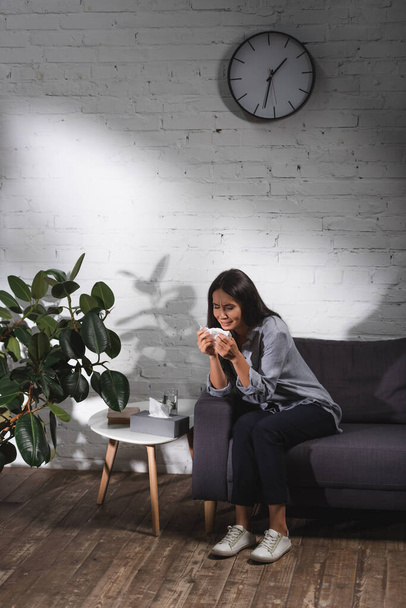 Erwachsene Frau sitzt auf Couch und weint neben Couchtisch mit Servietten - Foto, Bild
