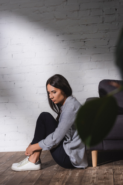 sad, lonely woman sitting on floor near brick wall at home, mental health concept - Фото, зображення