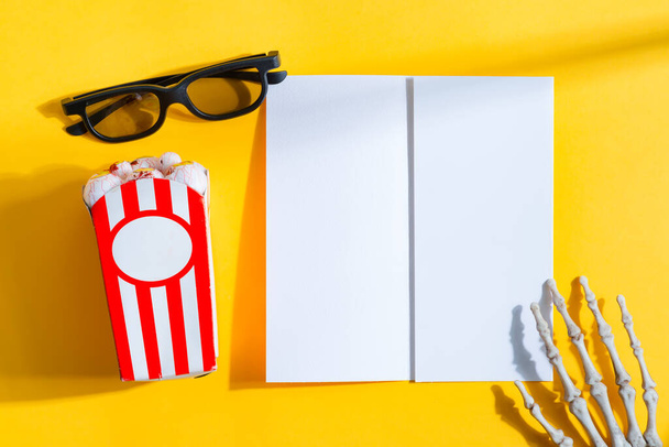 Set for watching movies at cinema - glasses, Halloween corn in the shapes of eyeballs and paper mock-up bifold ticket on a yellow background, copy space. Top view. Helloween concept. - 写真・画像