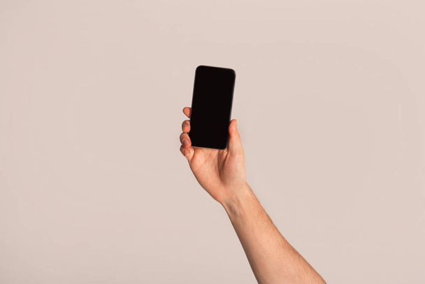Cellphone with empty screen in male hand on light background, space for design - Foto, afbeelding