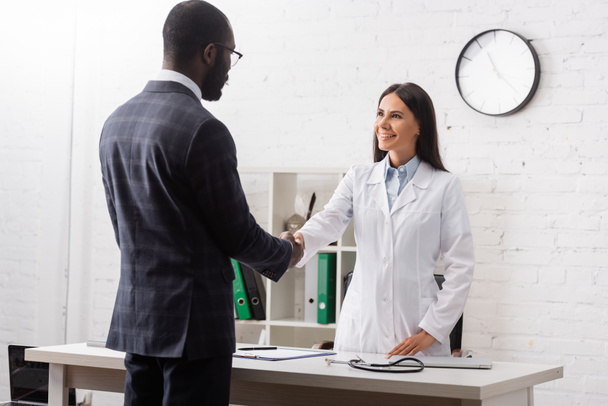brunette woman shaking hands with african american patient wearing suit - Photo, Image