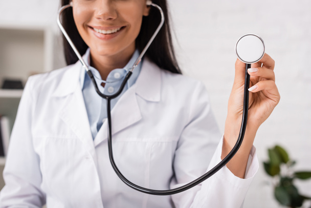bijgesneden weergave van vrolijke arts die stethoscoop in kliniek - Foto, afbeelding
