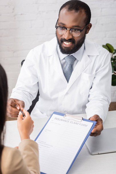 selective focus of african american doctor giving pen and insurance claim form to patient - Foto, Bild