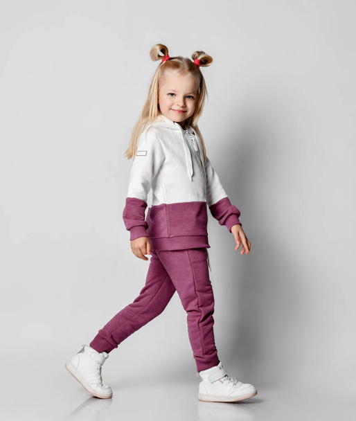 Little blonde girl in a sports suit posing on a gray background. - Foto, Imagem