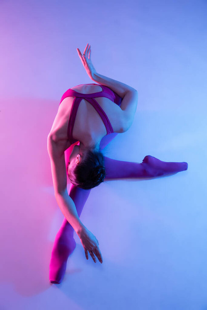 Young and graceful ballet dancer isolated on purple studio background in neon light - Fotó, kép