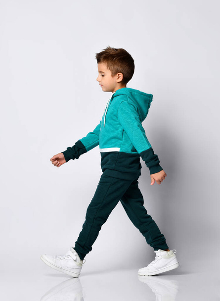 Little brunette boy in a sports suit posing on a gray background. - Photo, Image