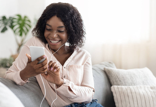 自宅でスマートフォンやリスニング音楽で陽気な黒の女の子のメッセージング - 写真・画像