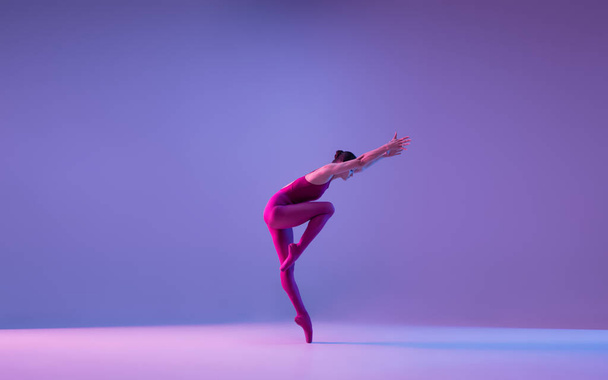 Young and graceful ballet dancer isolated on purple studio background in neon light - Foto, Imagem