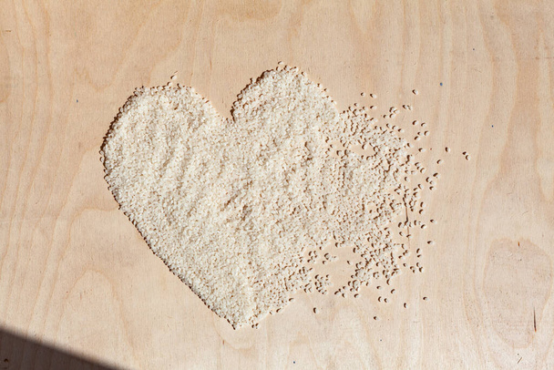 Ryżowe serce na drewnianym tle z miejscem na napis. Symbol serca zrobiony z ryżu. Serce zrobione z płatków. Zdrowe odżywianie - Zdjęcie, obraz