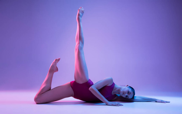 Young and graceful ballet dancer isolated on purple studio background in neon light - Foto, Bild