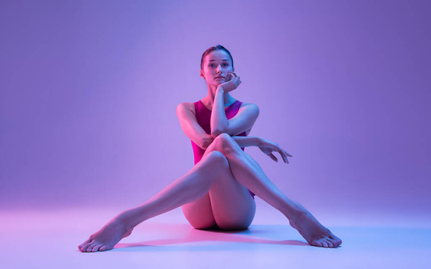 Jovem e graciosa bailarina de balé isolado em fundo estúdio roxo em luz de néon - Foto, Imagem