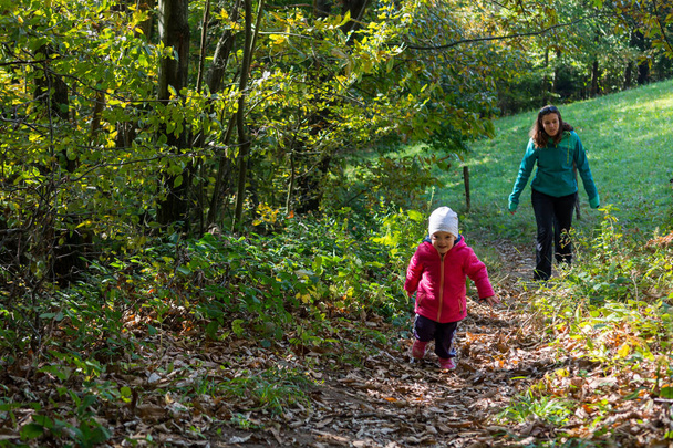 Daughter running infornt of her mother on a forest path. - Photo, Image