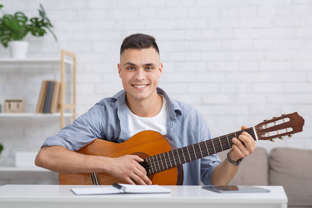 Smiling guy with guitar, tablet and notebook plays and writes songs - Fotografie, Obrázek