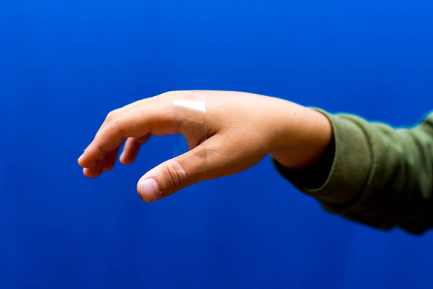 Boy human hand an adhesive transparent tape is glued to it.Blue studio background. - Photo, Image
