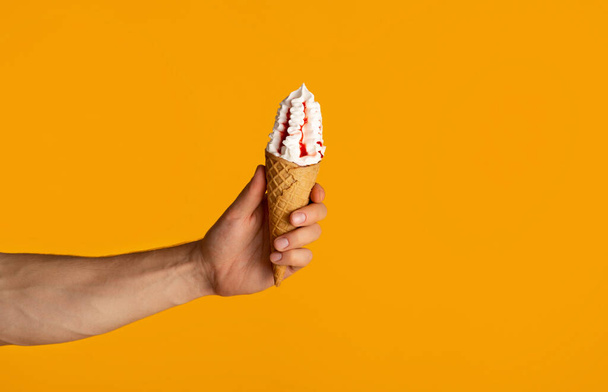 Cropped vue de millennial guy holding yummy ice cream in waffle cone sur fond orange, gros plan - Photo, image