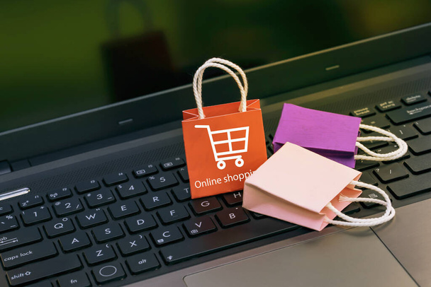 Small and colorful paper shopping bags on a laptop keyboard. Ideas about online shopping or shopping at home or office which customers can purchase items or services or goods remotely. - Photo, Image