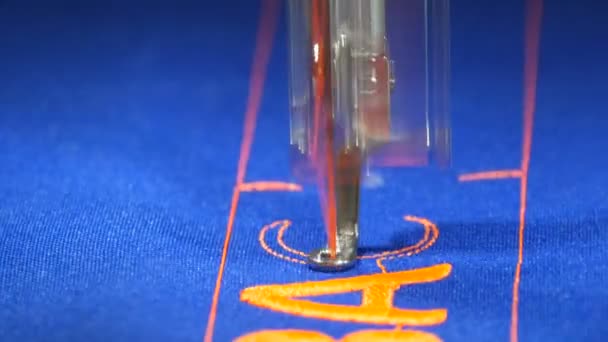 Een speciale naald van een naaimachine borduurt oranje letters op blauwe stof in een naaiatelier of naaiatelier van dichtbij bekijken - Video